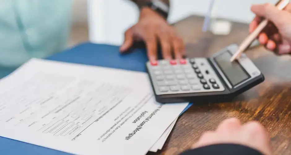 Hands using a calculator with real estate documents on a desk, indicating a financial transaction or meeting.