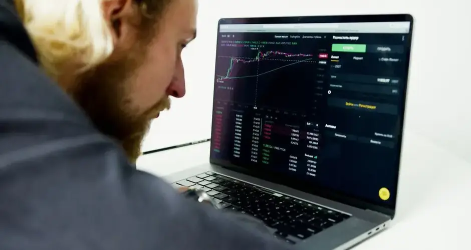 A focused man analyzing stock market data on a laptop, tracking investments and trading strategies.