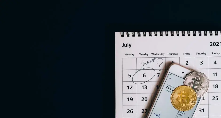 Top view of bitcoins and smartphone on July 2021 calendar, suggesting investment planning.