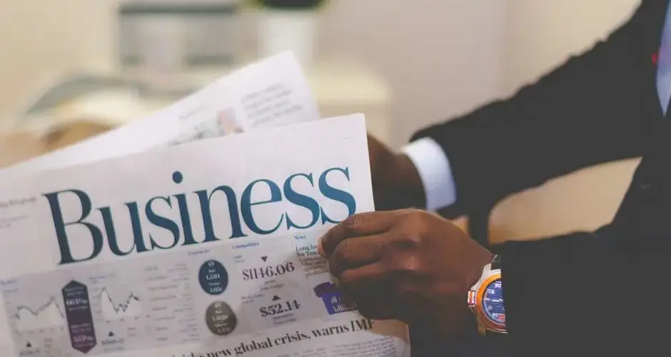 Close-up of a businessman reading a newspaper indoors, focusing on business headlines.