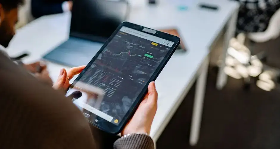 A person using a tablet for stock market analysis in an office setting.
