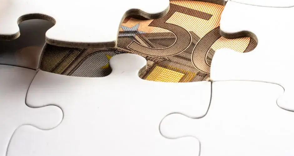 Close-up of a partially completed puzzle revealing a Euro note underneath, symbolizing financial discovery.