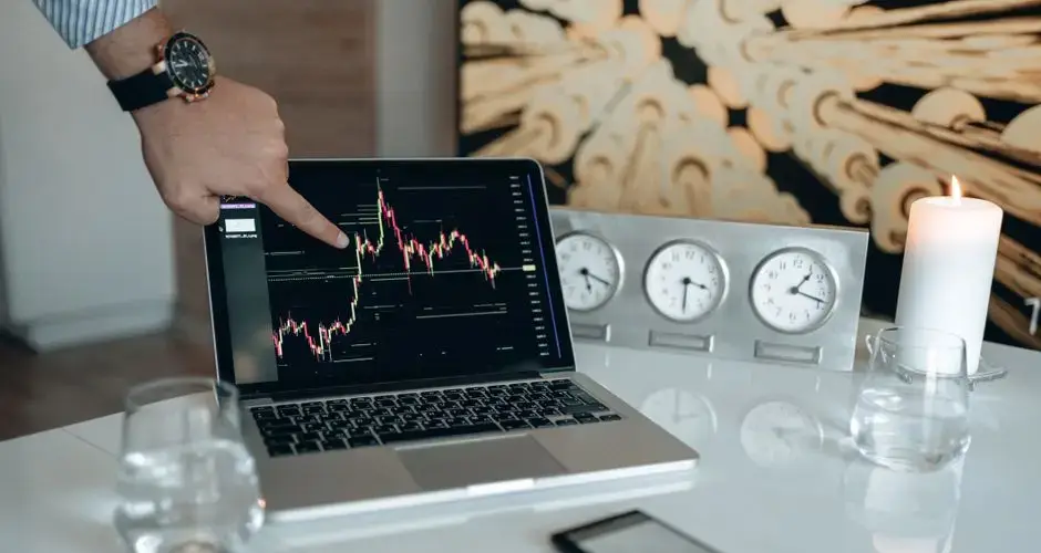 A businessman points to a stock chart on a laptop screen, indicating market analysis insights.