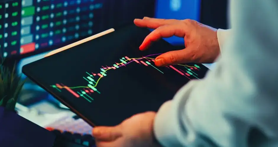 A close-up of a person using a tablet to analyze stock market trends and charts indoors.