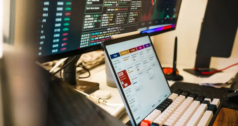 A sleek, modern workspace featuring trading monitors and a tablet for project management.