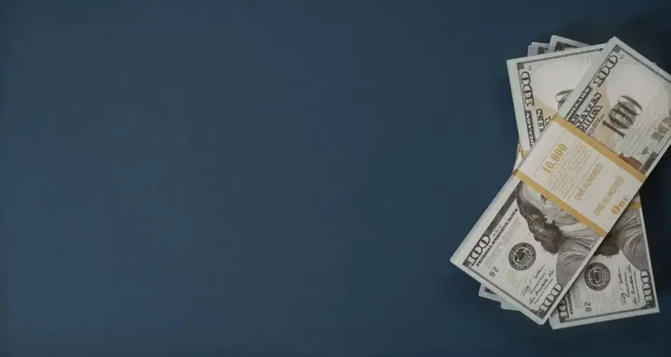 A bundle of US dollar bills on a dark blue background with ample copy space.