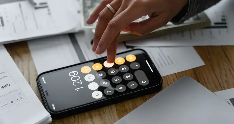 Close-up of a person using a smartphone calculator on a table with documents for financial calculations.