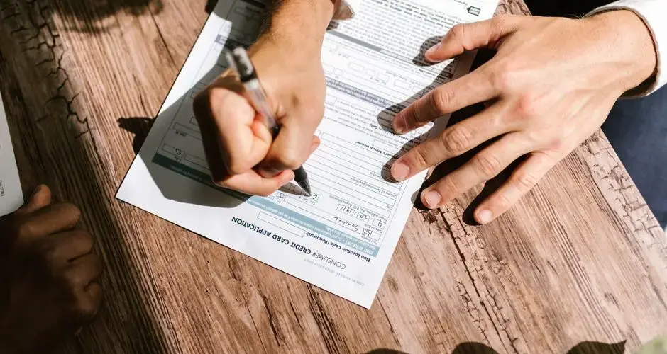 Hands writing on a consumer loan credit application form on a wooden table.
